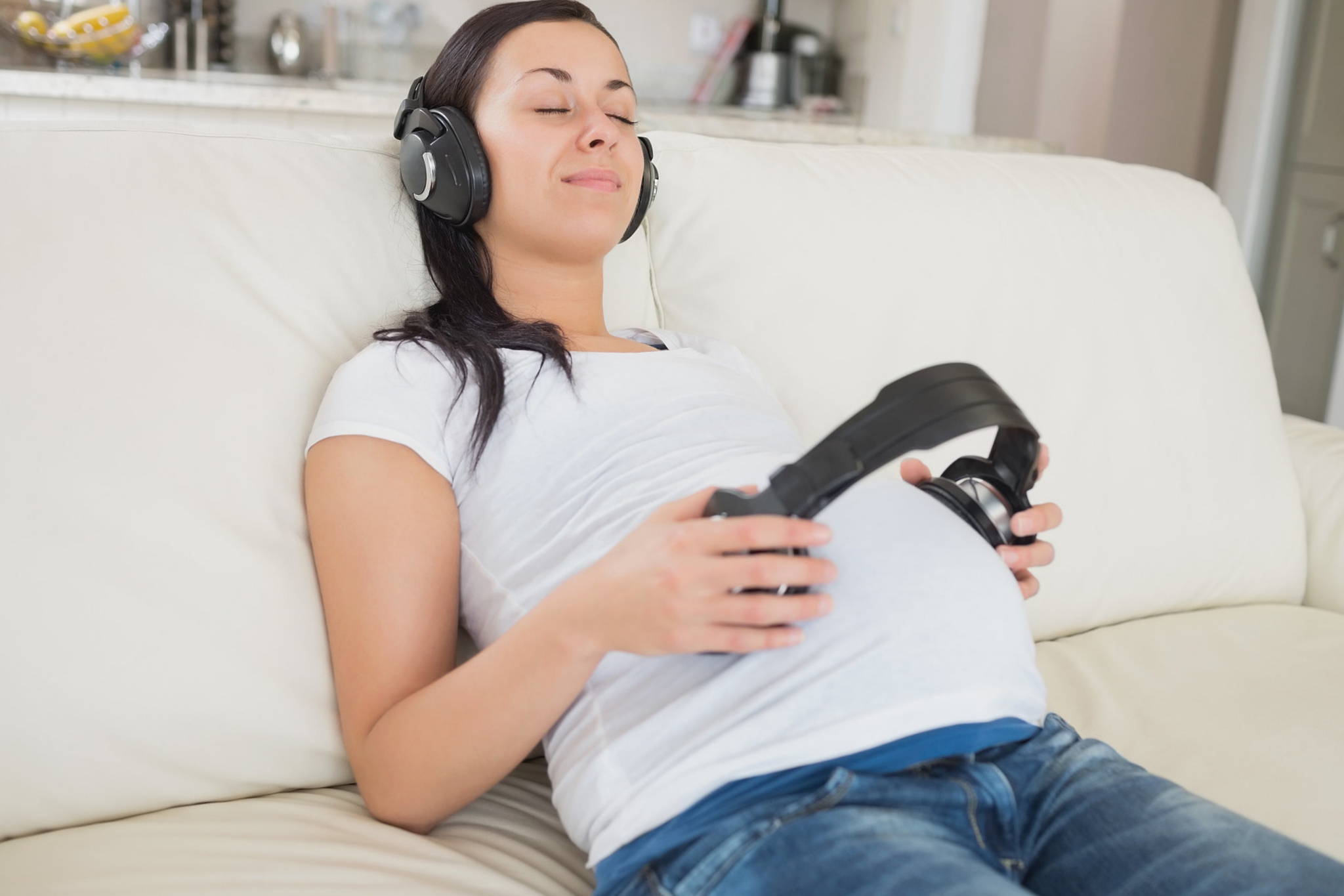 Беременная в наушниках слушает музыку